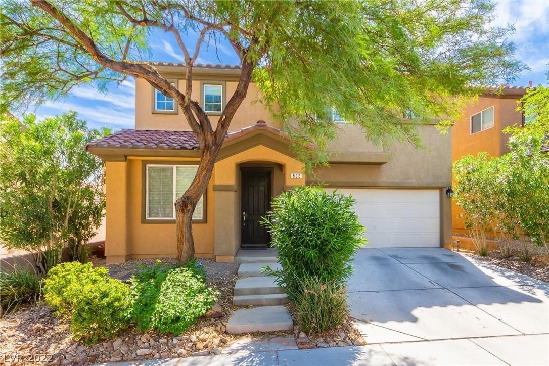 A warm-toned beige stucco home with tile roofing, bushes and trees out front